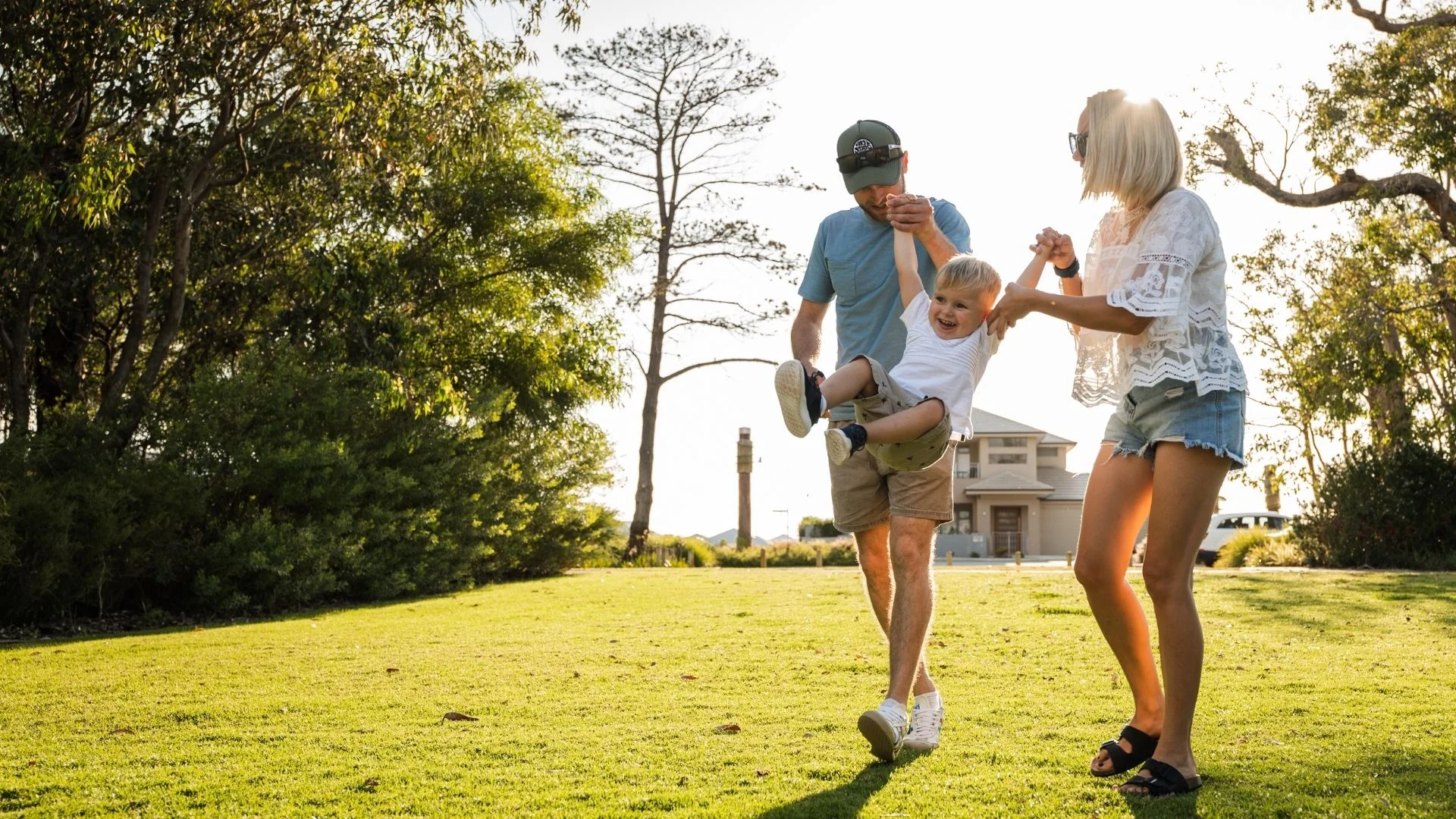 A couple walking with their toddler son in a park, each holding one of his arms while 'flying' him playfully.