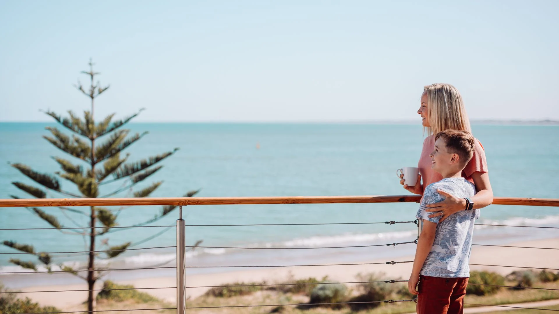 A blond-haired mother and her young son on a balcony overlooking the ocean in Mandurah.