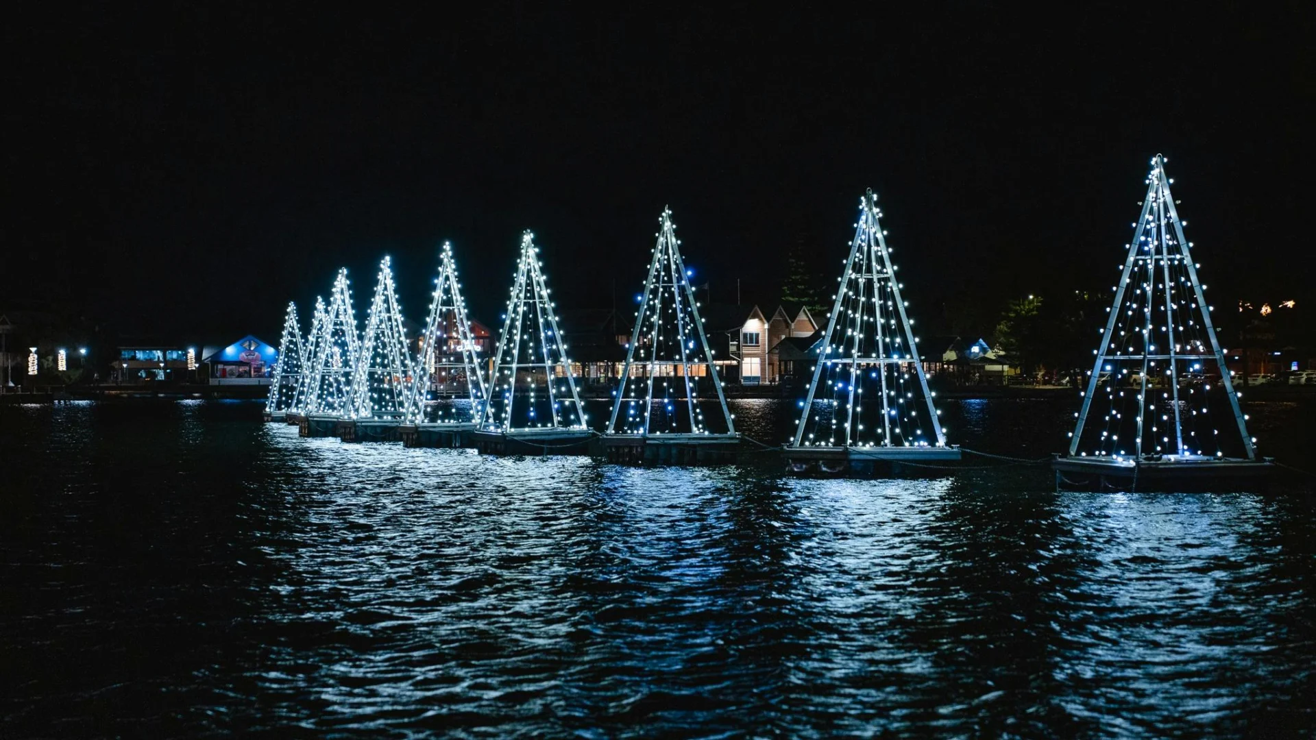 Glowing floating Christmas tree installations reflecting on the water.