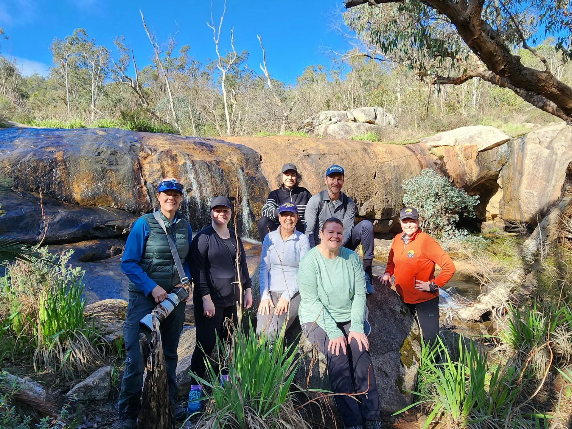 Group of smiling hikers standing in front of waterfall in Serpentine NP