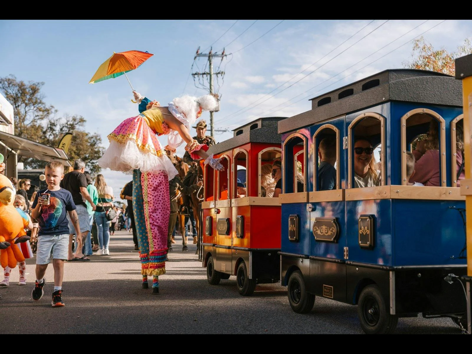 Rainbow stiltwalker greeting kids on a rainbow train