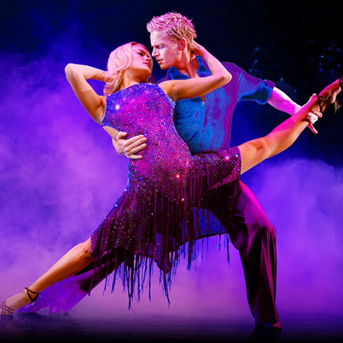 A couple performs an elegant dance pose on stage, surrounded by purple smoke. The woman wears a sparkling purple dress and high heels, while the man wears a blue shirt and purple pants.