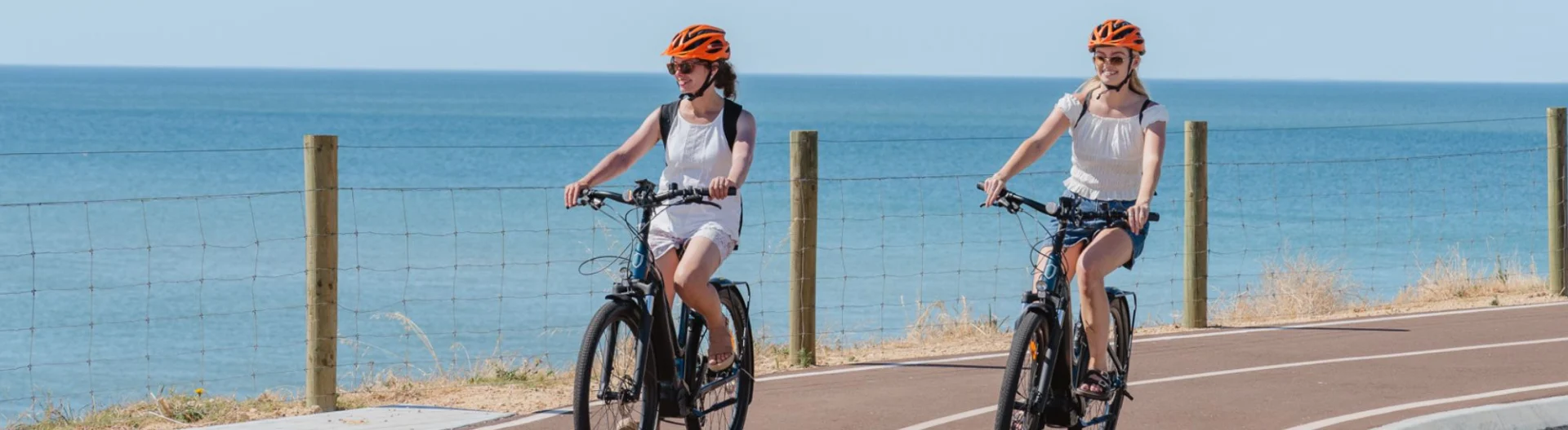 Two womens ride bicycles along the coast with the ocean in the background.