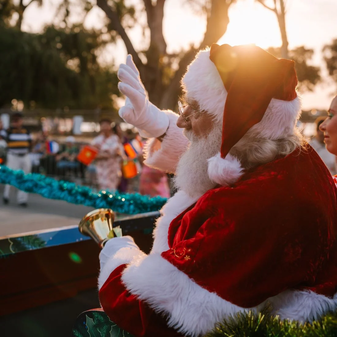 Santa Claus waving and holding a gold bell while riding on a float.