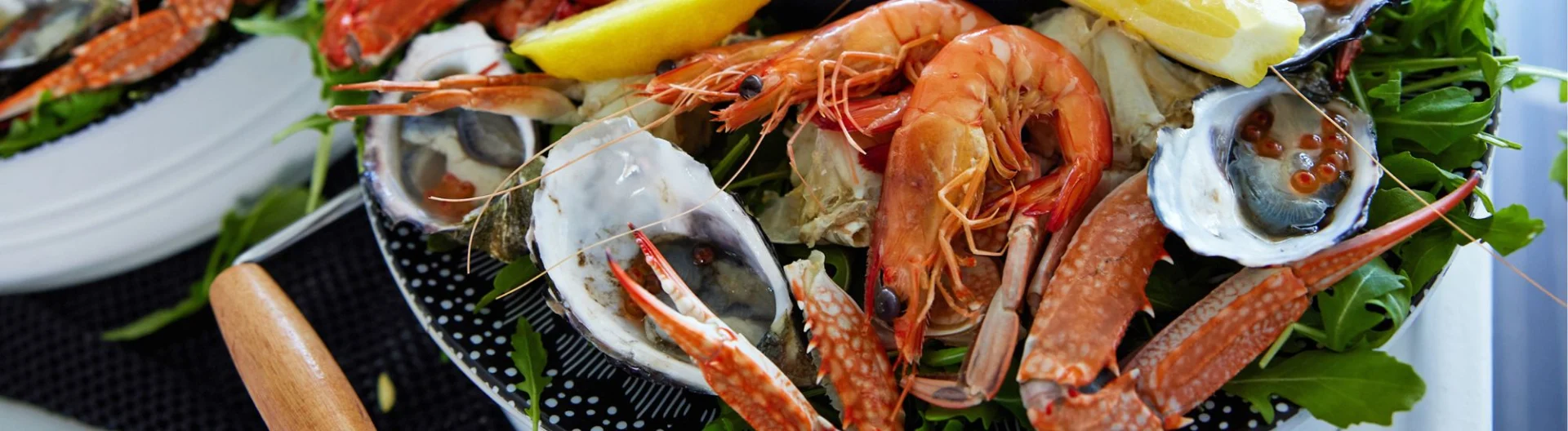 A close-up of a seafood platter with prawns, oysters with roe, crab legs, and lemon wedges, served on a bed of fresh greens.
