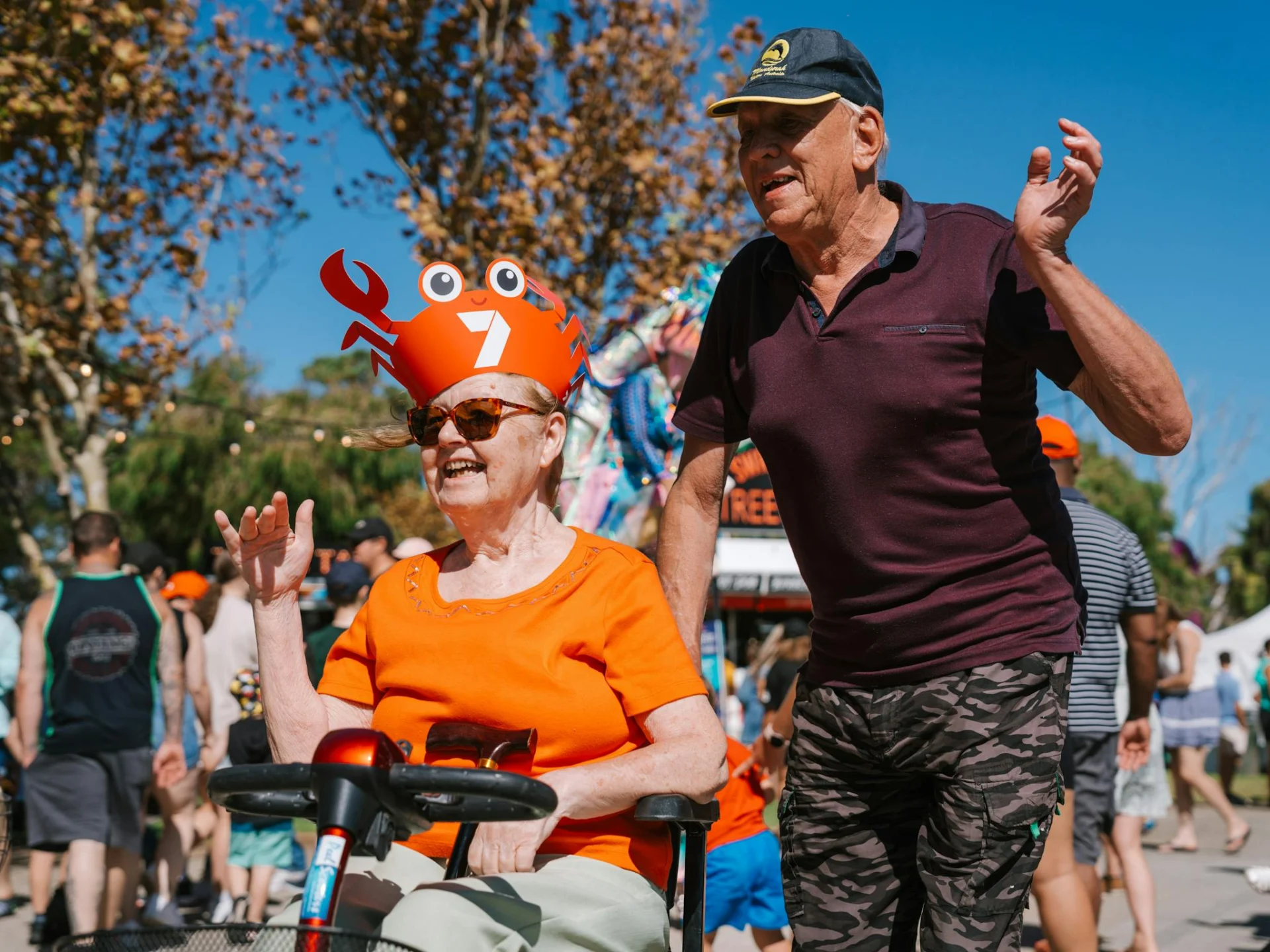 Woman sitting on scooter and man walking next to her smiling and waving