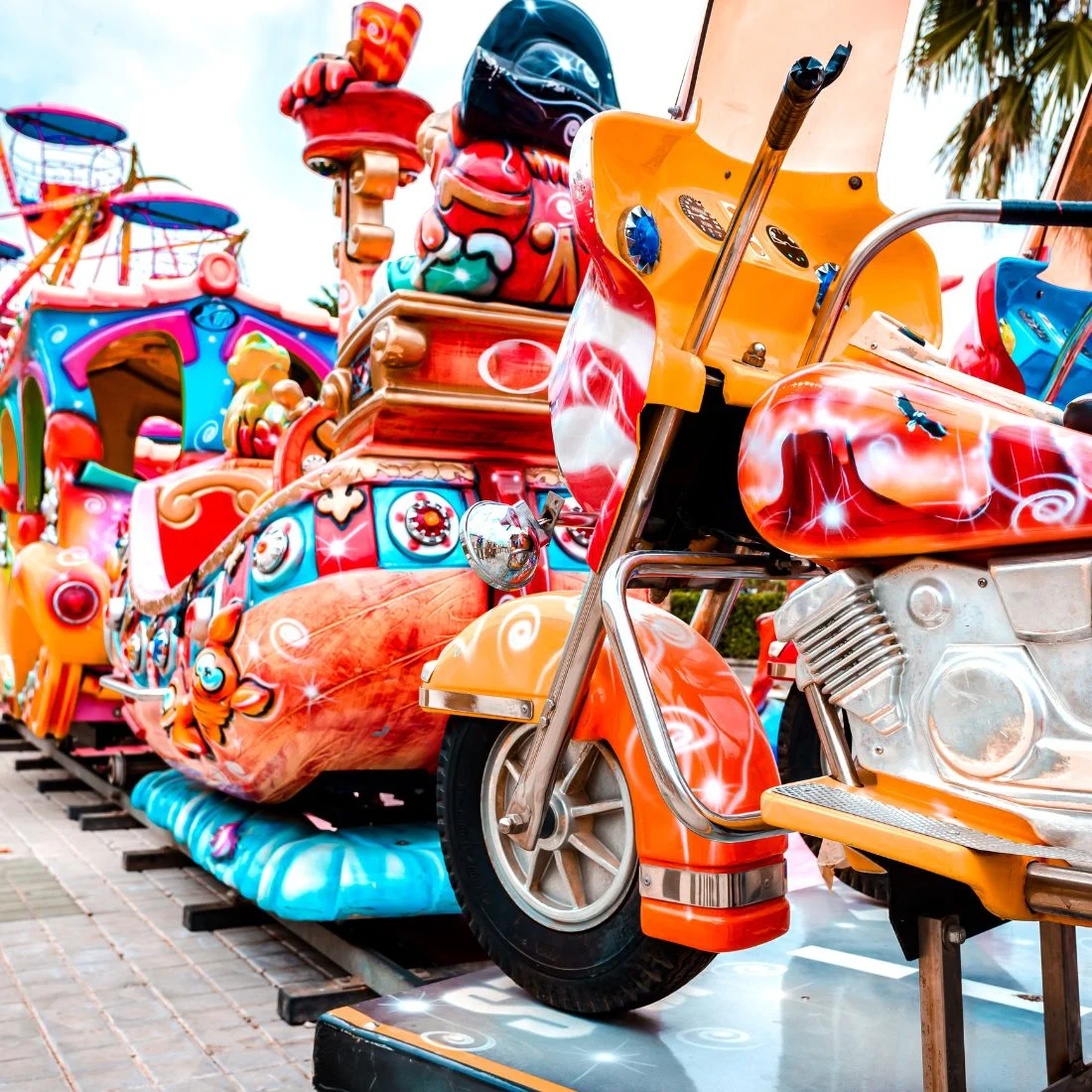 A colourful amusement park ride with several motorcycle-themed cars attached to a train on tracks.
