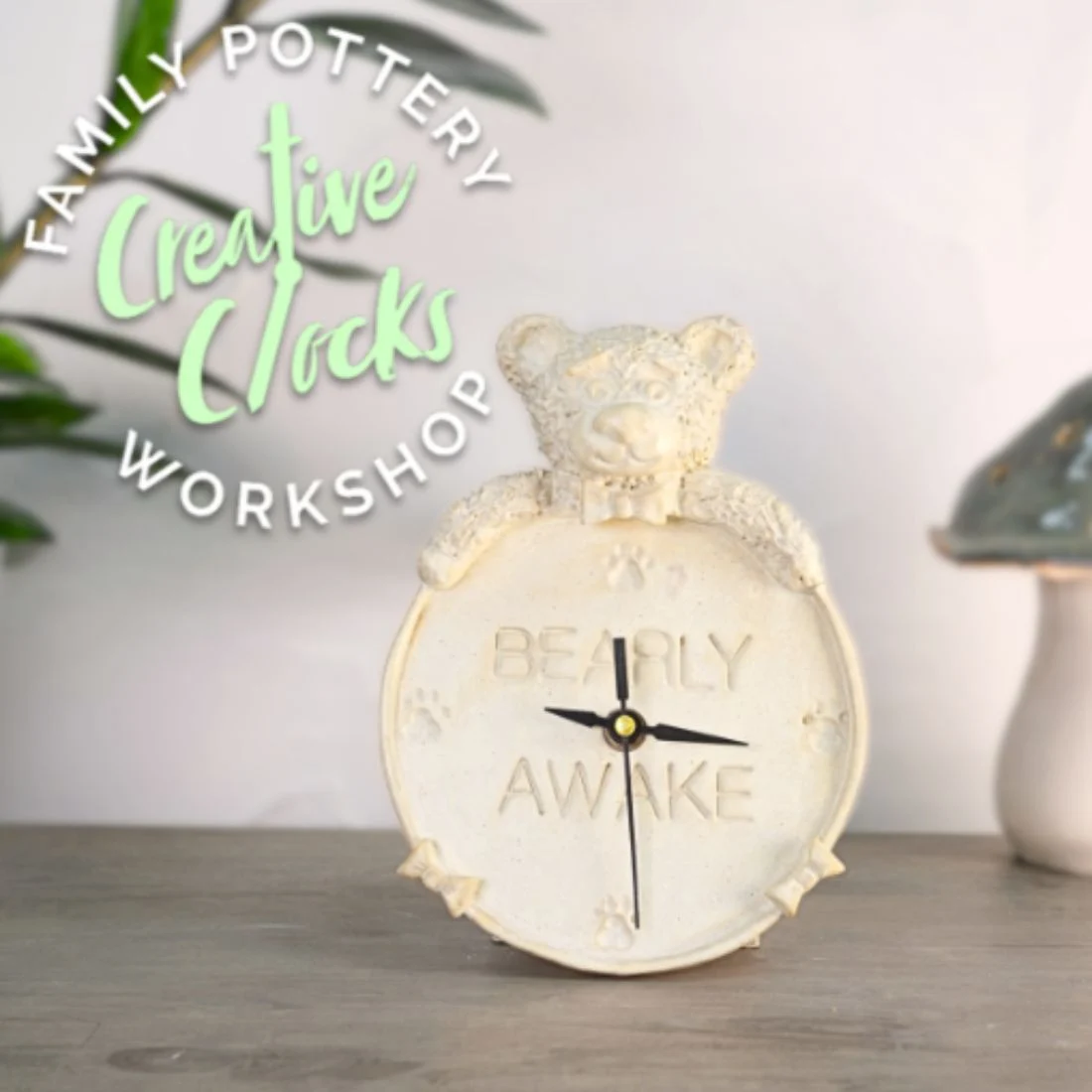 A handmade pottery clock shaped like a bear with the words Bearly Awake is displayed on a table. Text reads Family Pottery Creative Clocks Workshop. Green plant and ceramic mushroom are in the background.