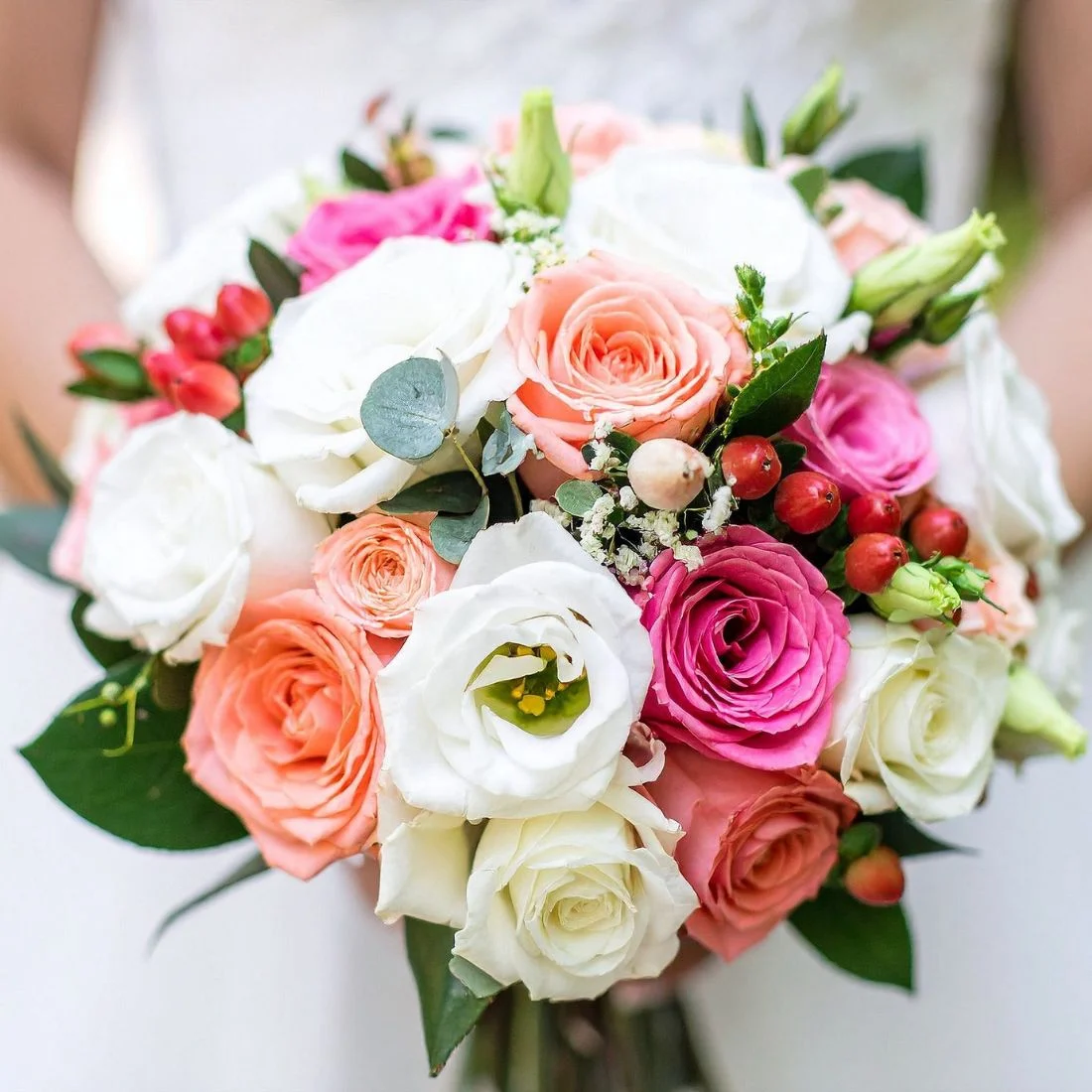 A bouquet of roses in shades of pink, peach, and white, accented with red berries and greenery.