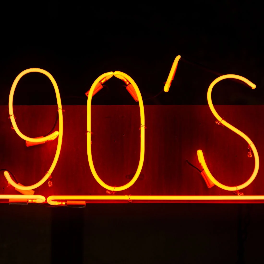 Neon sign that reads "90's" in bright yellow against a dark background with a red glow.