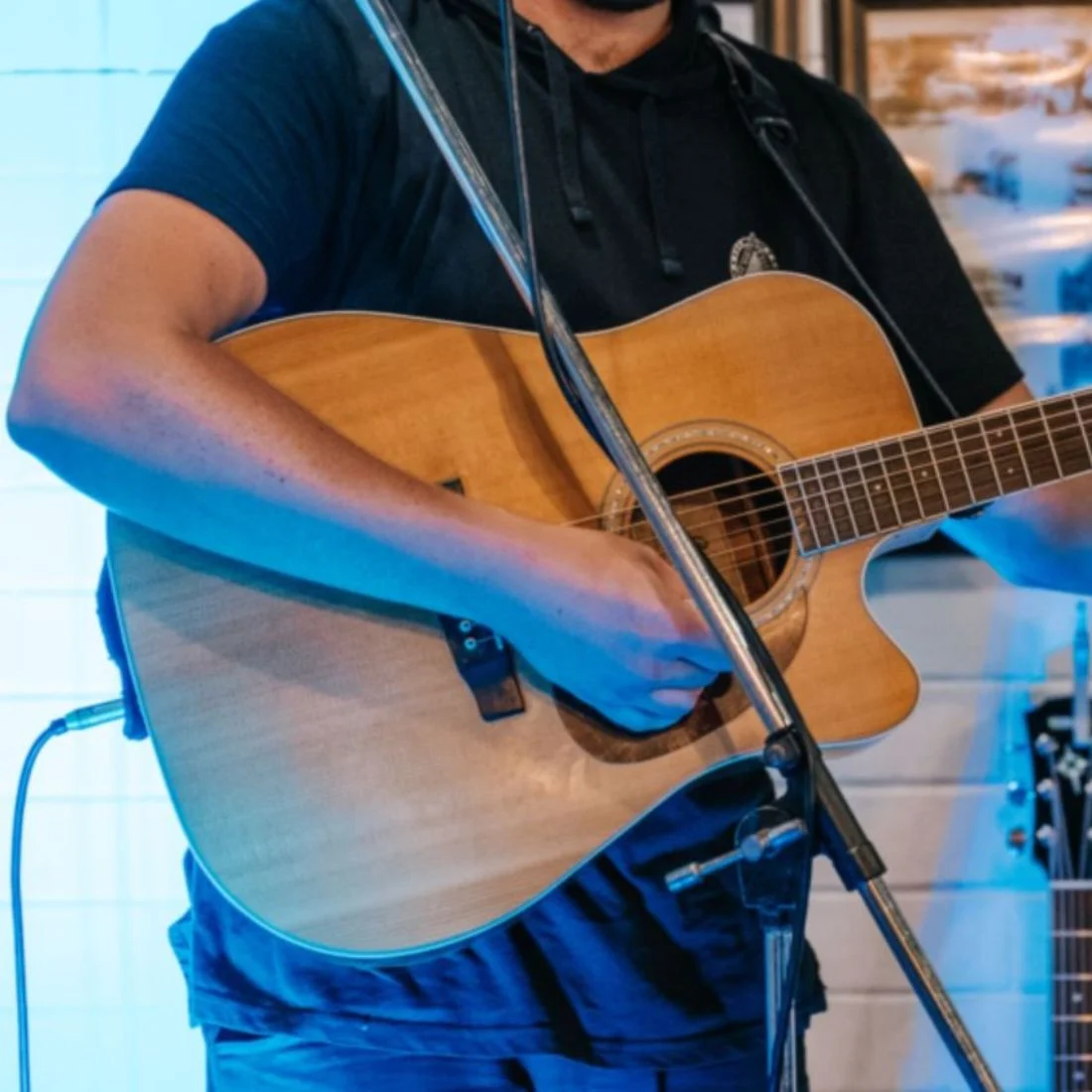 A person plays an acoustic guitar, illuminated by blue stage lighting.