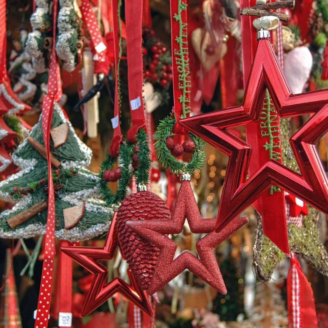 Red star ornaments, heart-shaped decorations, and small Christmas tree ornaments hang among other festive décor items at a holiday market stall.