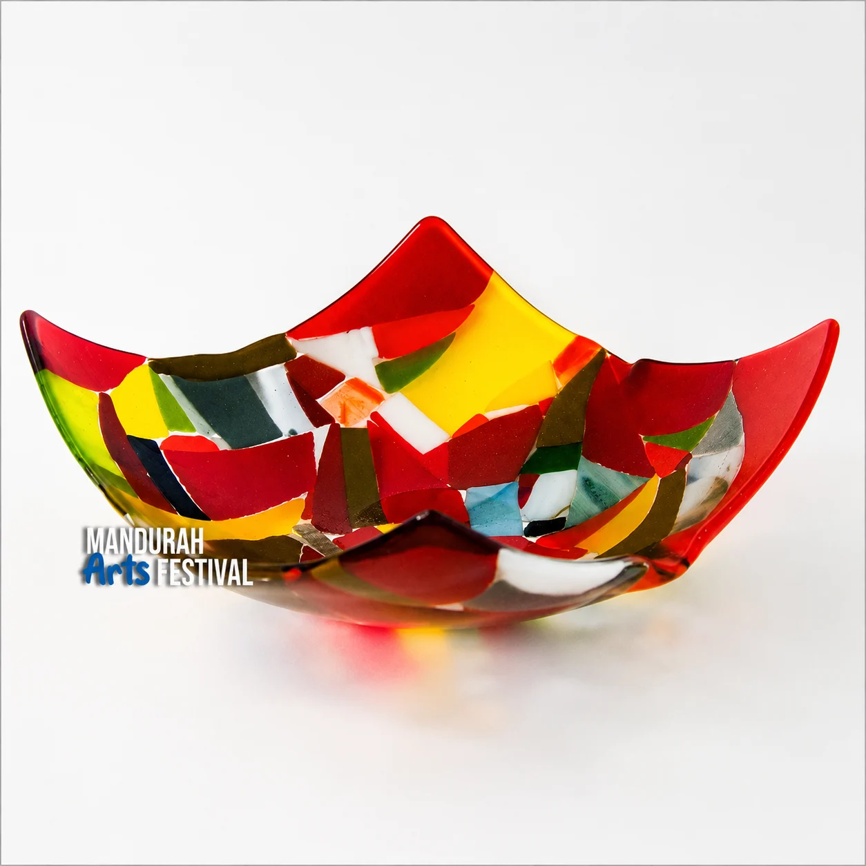 A colorful, abstract glass bowl with a scalloped edge, featuring red, yellow, green, and white shapes. The Mandurah Arts Festival logo is on the left side. The bowl is placed on a white background.