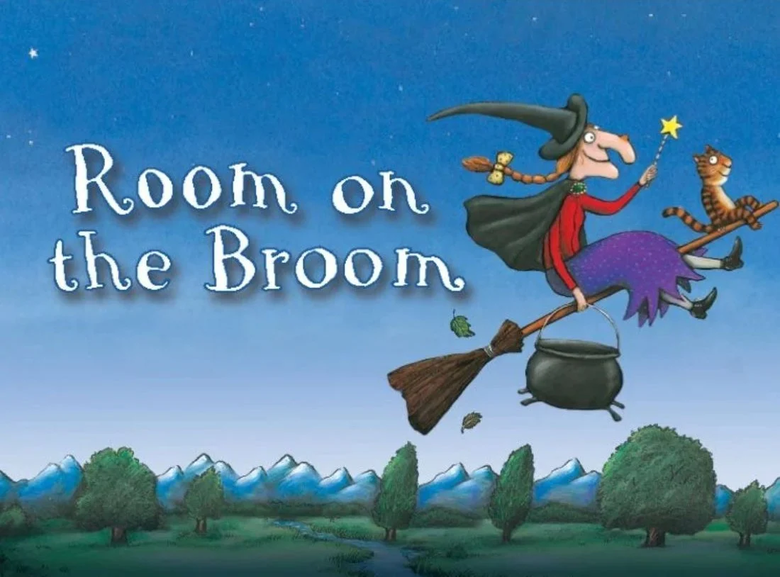 Illustration of a smiling witch with a cat, flying on a broomstick above trees and mountains. The witch holds a wand, and the words Room on the Broom are in large white letters on the sky.