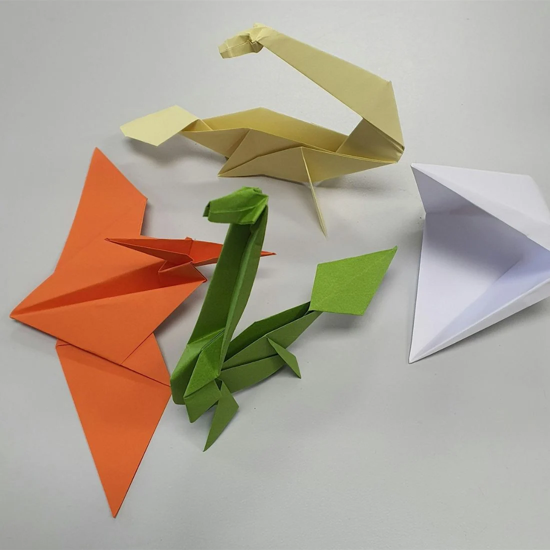 Colourful paper animals and folded paper shapes in orange, green, yellow, and white scattered on a light gray surface.