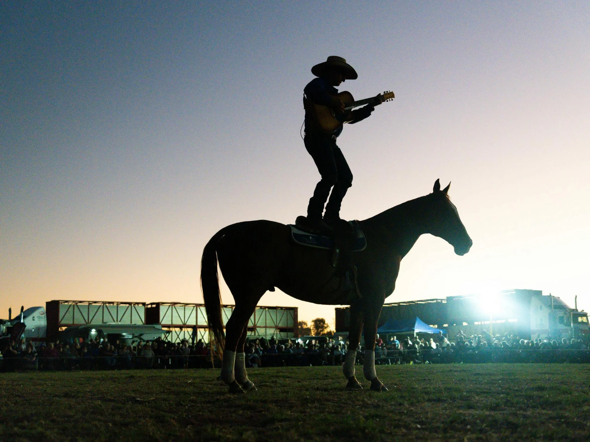 Tom Curtain standing on a horse while playing guitar and singing a song