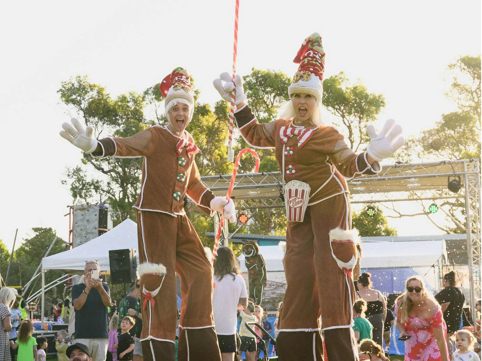 Two stiltwalkers dressed as gingerbread men waving to the camera