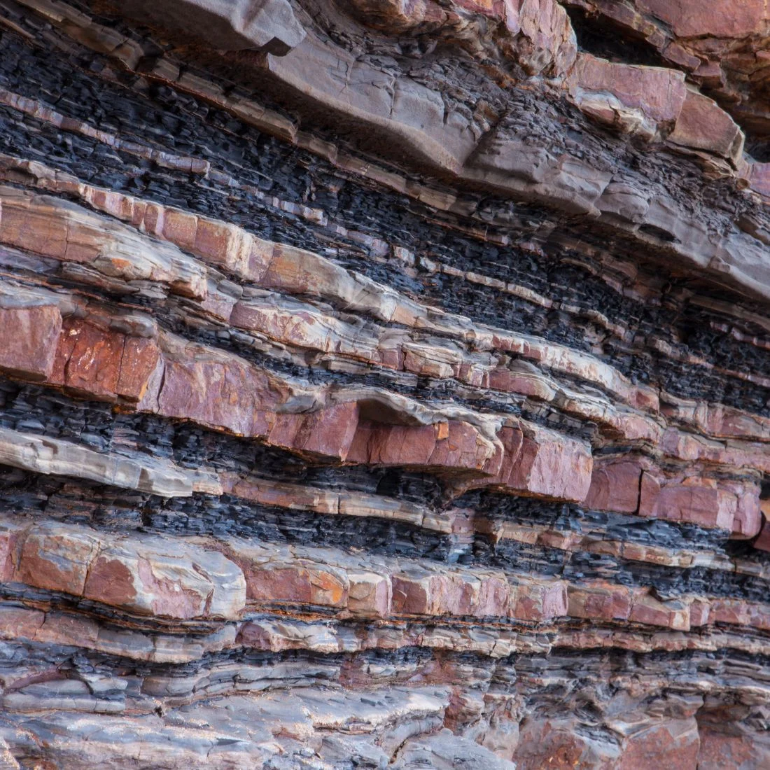Layered rock formation with alternating reddish and dark strata, showing clear geological bands and textures.