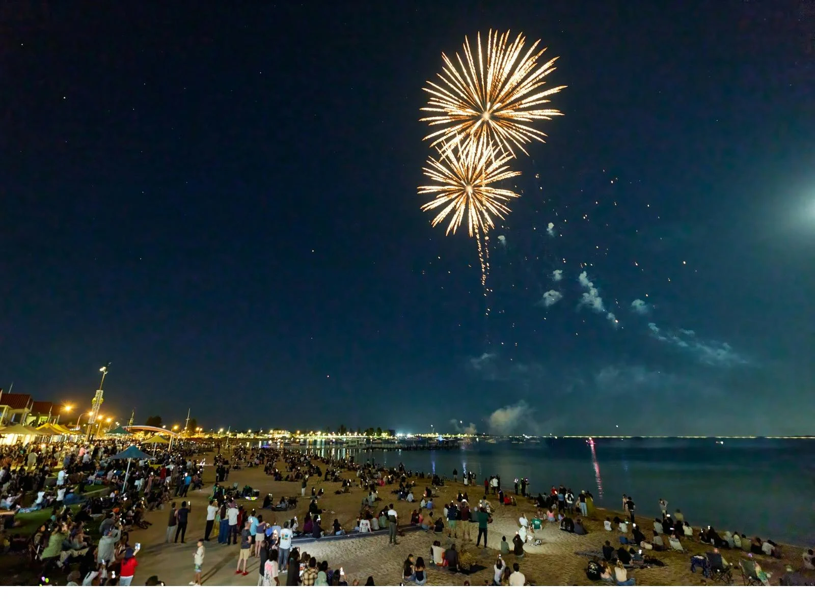 Golden fireworks exploding over a beach full of viewers