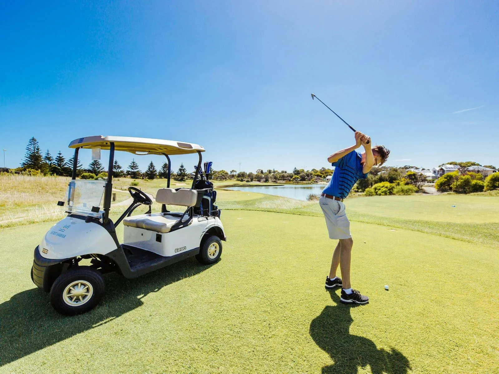 Man swinging a golf club next to golf cart