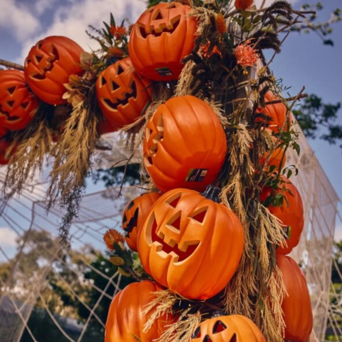 A decorative arch adorned with orange plastic jack-o-lanterns, dried grasses, and wispy faux spiderwebs.